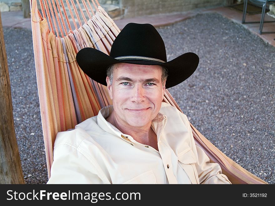 A smiling man with beautiful green eyes wearing a cowboy hat and resting in a hammock. A smiling man with beautiful green eyes wearing a cowboy hat and resting in a hammock.