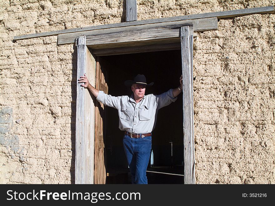 A man with wearing a cowboy hat standing in the door of an old weathered adobe building. A man with wearing a cowboy hat standing in the door of an old weathered adobe building.