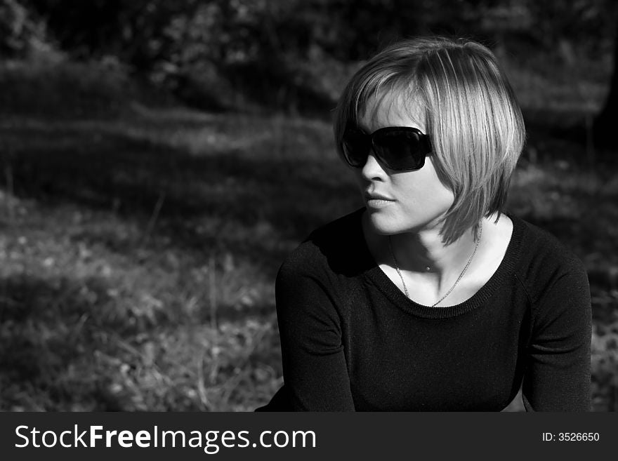 Pretty young woman in sunglasses dreaming sitting in the park
