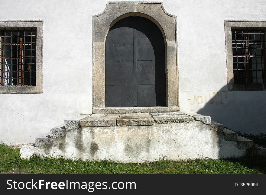 A detail of an old door wit stony stairs leading up to them and two grilled windows