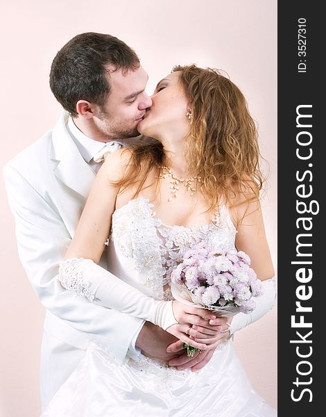 Young couple kissing in wedding wear with bouquet of chrysanthemum. Special pink toned photo f/x. Young couple kissing in wedding wear with bouquet of chrysanthemum. Special pink toned photo f/x