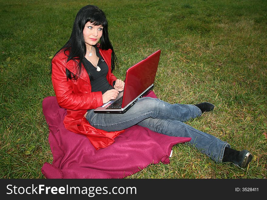 Black head woman is sitting on a plaid in park grass with notebook