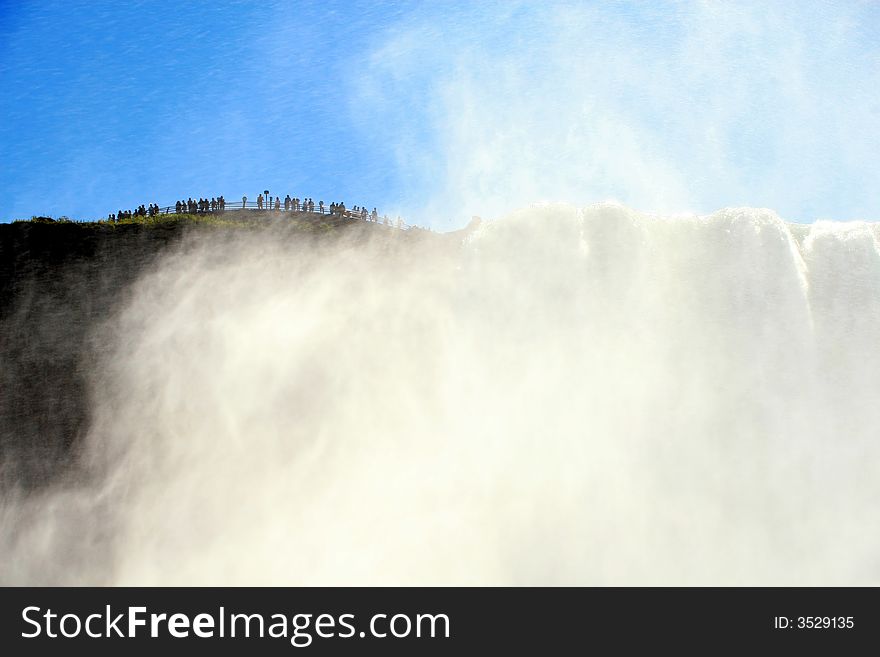 A dramatic river view of tourists watching over the American Falls at Niagara. A dramatic river view of tourists watching over the American Falls at Niagara.