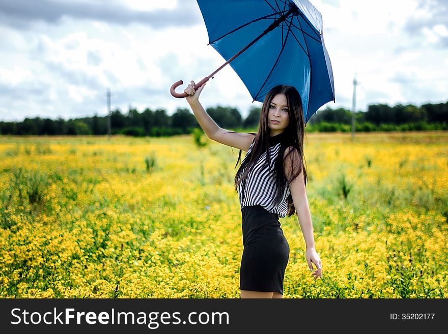 Slim Girl Standing With Blue Umbrella In Yellow Flowers Field