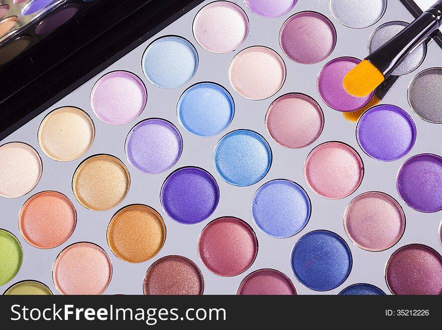 Open compact of colourful eye shadow with multiple small round containers in different colours together with a small applicator or brush, view from above