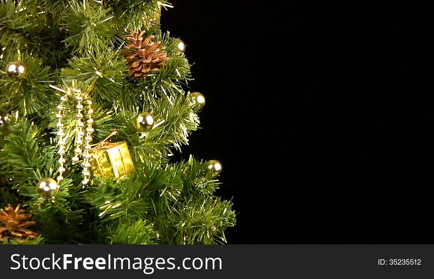 Green Christmas tree (part of) with gold ornaments rotates on a black background. Green Christmas tree (part of) with gold ornaments rotates on a black background