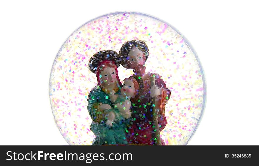 Joseph and Mary with baby Jesus in her arms. Glass ball with toy figures on a white background. The blizzard of multicolored sequins. Joseph and Mary with baby Jesus in her arms. Glass ball with toy figures on a white background. The blizzard of multicolored sequins