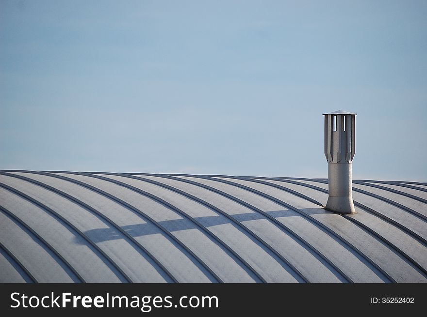 A modern chimney on top of a recent building with its shadow