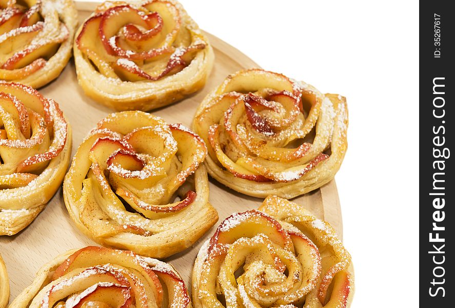 Sweet rolls with apples in the form of roses on wooden board on white isolated background