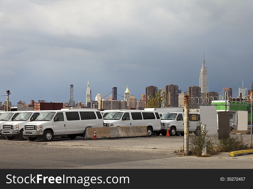 A parking lot with white vans infront of the New York City sky line on a cloudy afternoon. A parking lot with white vans infront of the New York City sky line on a cloudy afternoon.