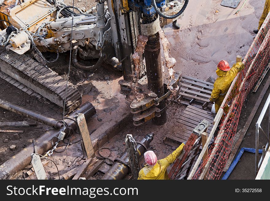 A group of workers assemble around a drilling machine and watch as mud sprays out. A group of workers assemble around a drilling machine and watch as mud sprays out.