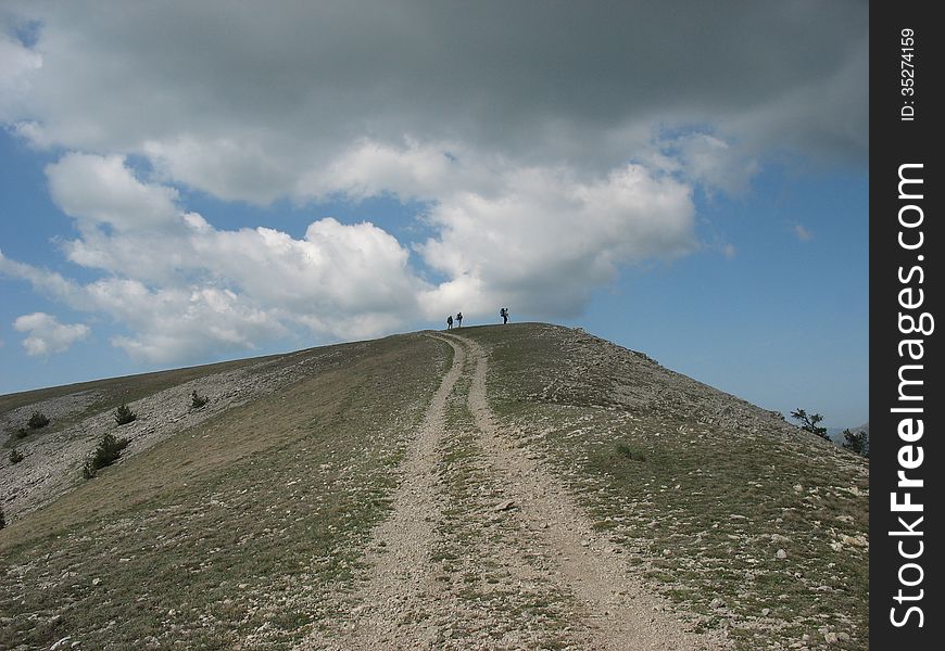 The road to the top of the mountain on the background of a contrasting sky with clouds. The road to the top of the mountain on the background of a contrasting sky with clouds