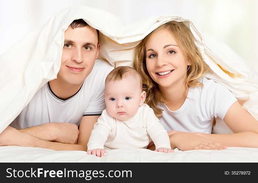 Happy family in bed under a blanket. mother, father, baby
