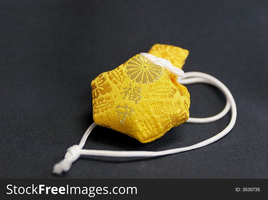 Closeup detail of a yellow asian religious charm on dark black cloth.