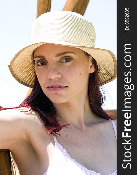 Beautiful woman with a summer hat sitting in the sun on a wooden swing.