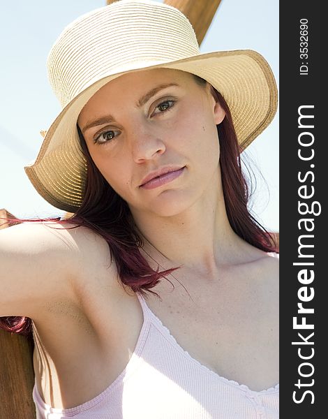 Closeup of a beautiful woman with a sun hat on, sitting on a wooden swing in the sunshine. Closeup of a beautiful woman with a sun hat on, sitting on a wooden swing in the sunshine.