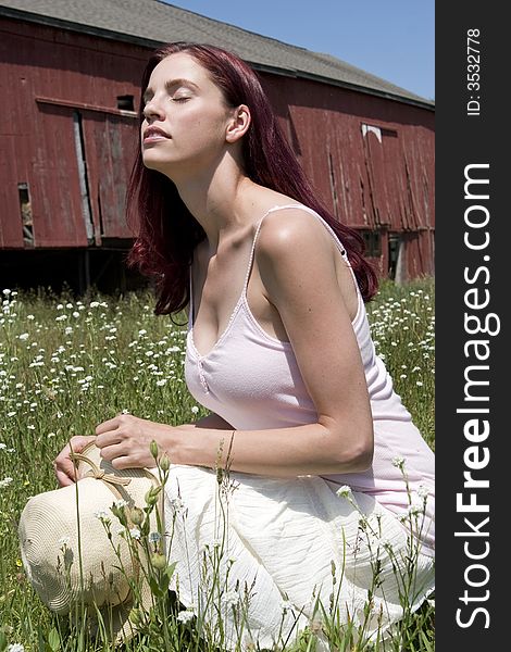 Pretty young woman kneeling with her eyes closed in a field of wild flowers with a red barn in the background. Pretty young woman kneeling with her eyes closed in a field of wild flowers with a red barn in the background.