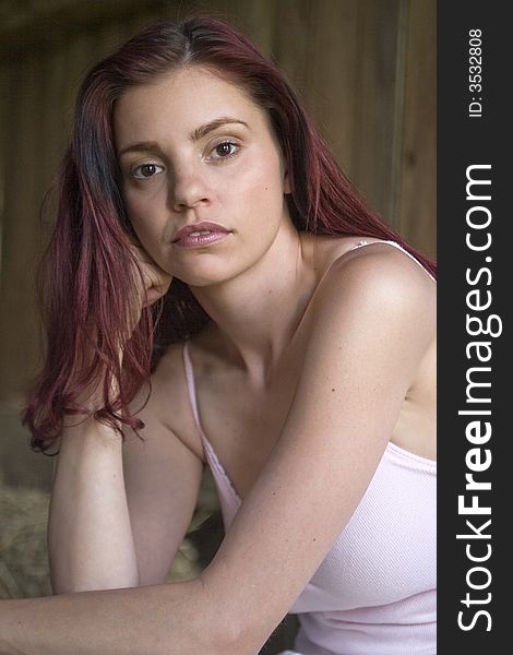 Beautiful young woman sitting in a sunlit barn looking thoughtful. Beautiful young woman sitting in a sunlit barn looking thoughtful.