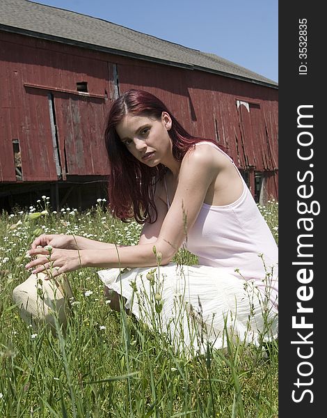 Beautiful young woman kneeling amid a field of wildflowers with an old barn in the background