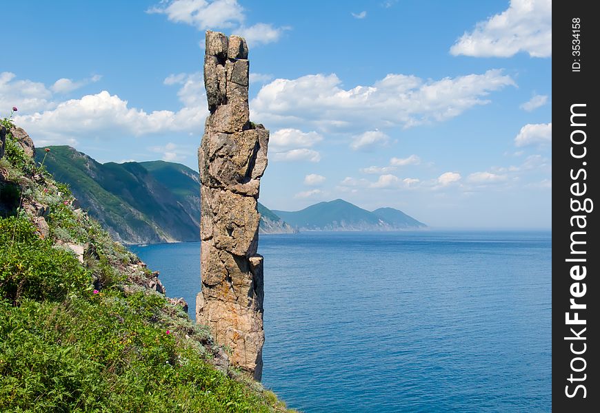 On foreground the single vertical rock with name Hare. On background turquoise sea, cliffs and sky with white clouds. Russian Far Easr, Primorye, Japanese sea, Tasovaya Bay. On foreground the single vertical rock with name Hare. On background turquoise sea, cliffs and sky with white clouds. Russian Far Easr, Primorye, Japanese sea, Tasovaya Bay.