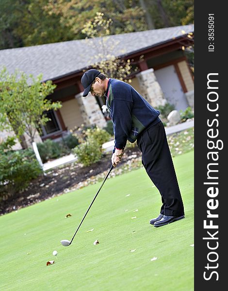 Man teeing off in front of the golf club house on a beautiful fall day. Man teeing off in front of the golf club house on a beautiful fall day.