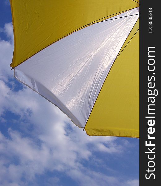 Part of a white-yellow parasol and a cloudy blue sky