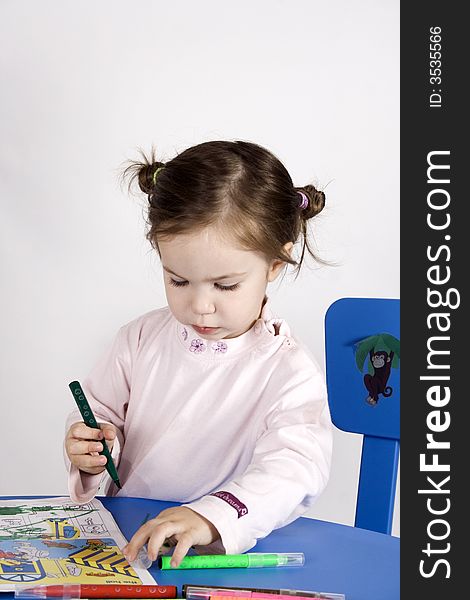 Little girl sitting on the chair and  writing on a  book