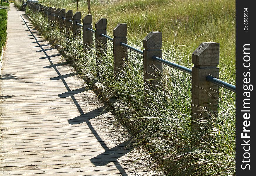 A boardwalk separated from a grassy sand dune by a low railing. A boardwalk separated from a grassy sand dune by a low railing.