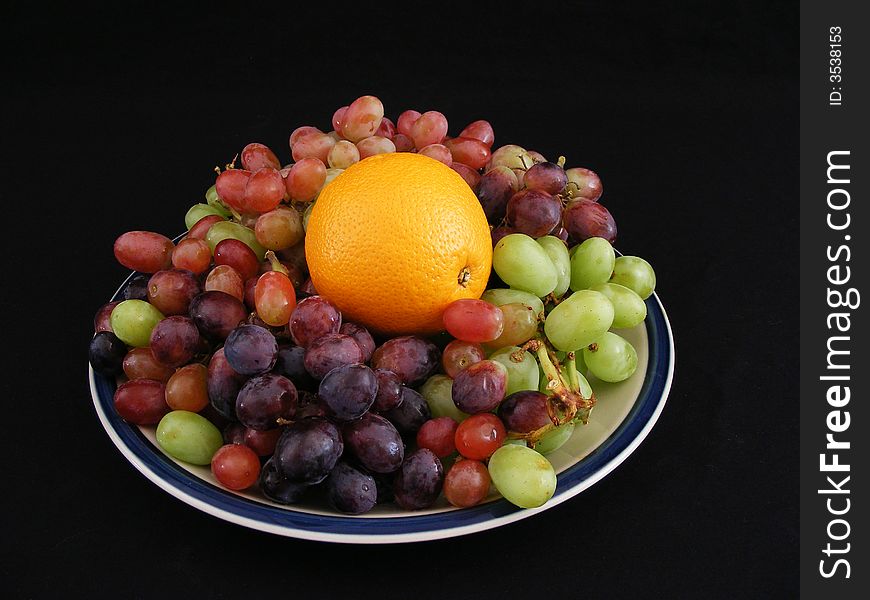 A navel orange on a bed of grapes against a black background. A navel orange on a bed of grapes against a black background.