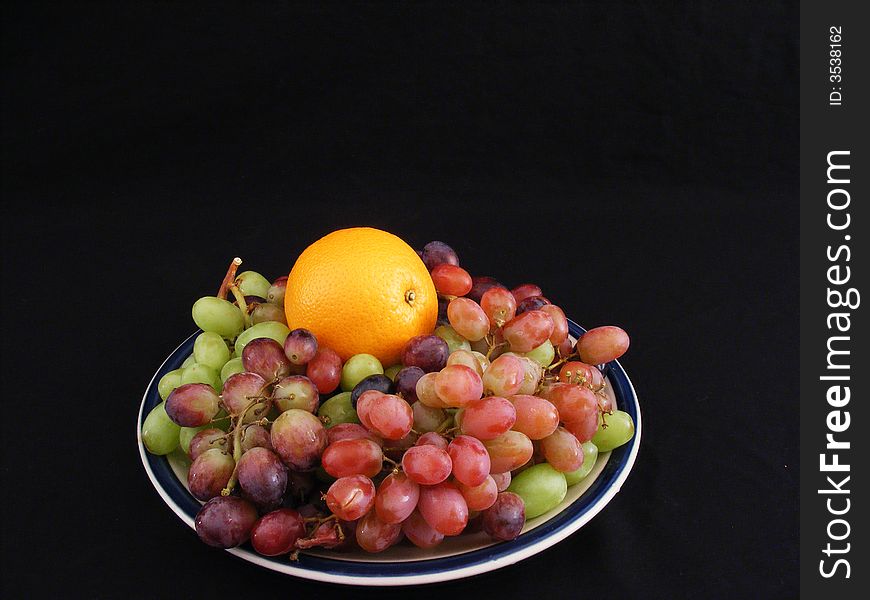 A navel orange on a bed of grapes against a black background. A navel orange on a bed of grapes against a black background.