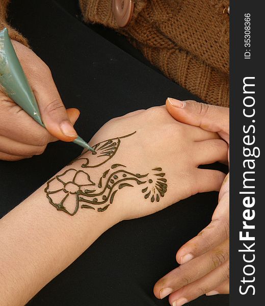 A woman creating a floreal henna design on the hand of a tourist in the desert of Dubai. A woman creating a floreal henna design on the hand of a tourist in the desert of Dubai
