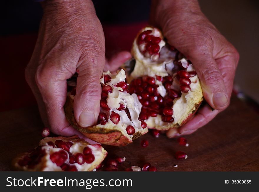 A man opens a pomegranate with its hand and the red seeds spread on the wooden table