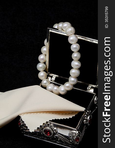 Pearl bracelet hanging on an open jewelry box on a black background