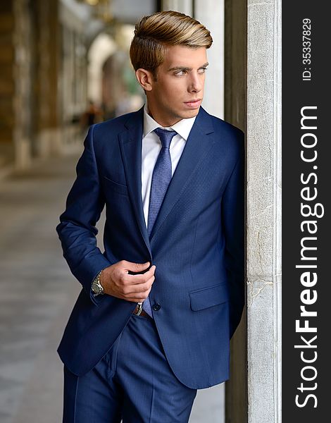 Portrait of an attractive young businessman in urban background wearing blue suit a necktie. Blonde hair