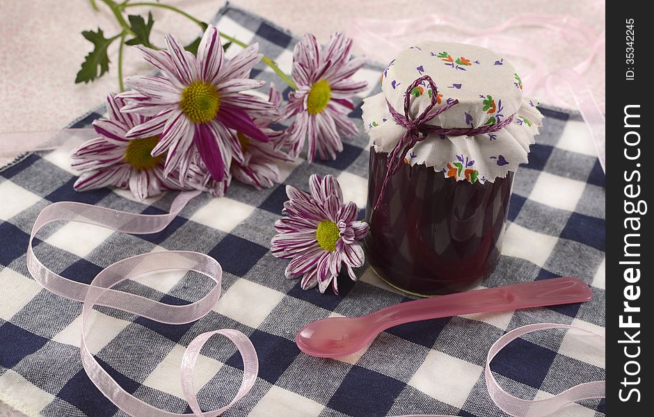 Jam jar with flowers and spoon on cute tablecloth