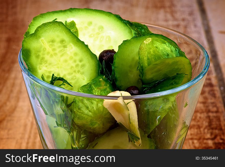 Appetizer with Slices of Delicious Pickled Cucumbers in Brine of Garlic, Dill, Parsley and Black Peppercorn in Glass Dish closeup on Wooden background