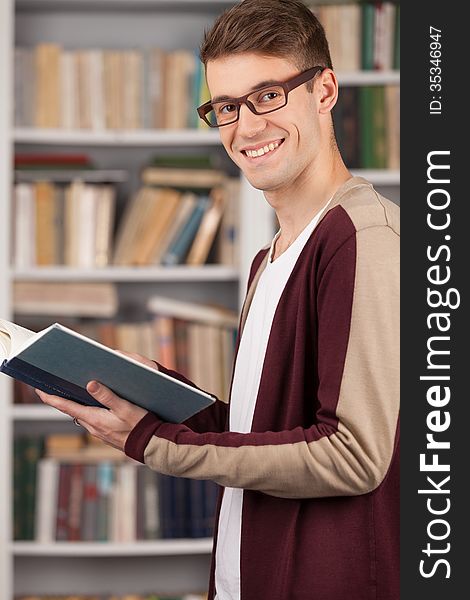 Side view of young man reading a book and smiling while standing at the library. Side view of young man reading a book and smiling while standing at the library