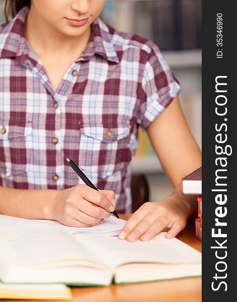 Young woman writing something in her note pad and reading book while sitting at the desk. Young woman writing something in her note pad and reading book while sitting at the desk