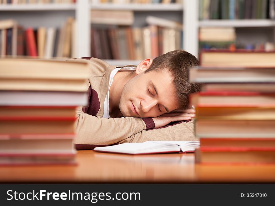 Tired young man sleeping near the book stacks at the library. Tired young man sleeping near the book stacks at the library