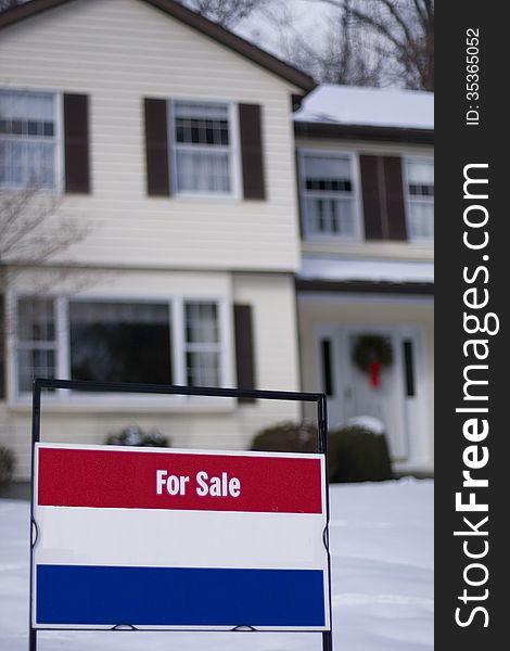 House for sale shown in the winter time covered with snow with real estate sign out front.