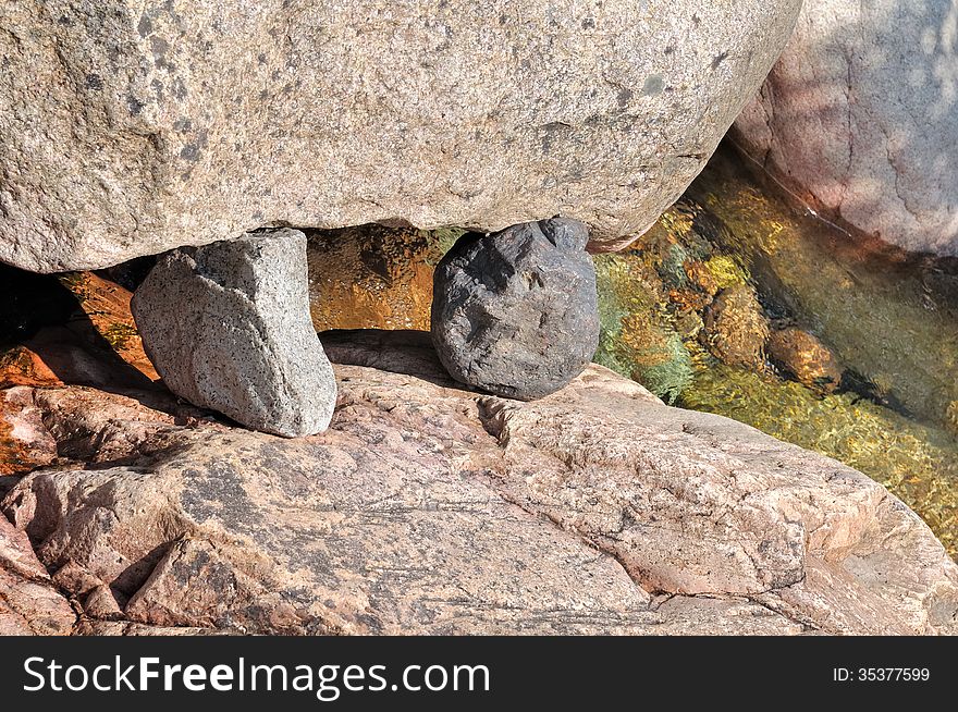 Two stones wedged between two blocks of granite in a river. Two stones wedged between two blocks of granite in a river