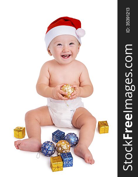 Little baby boy holding a bauble and wearing a red santa cap smiling and having fun with presents on the floor, isolated on white. Little baby boy holding a bauble and wearing a red santa cap smiling and having fun with presents on the floor, isolated on white