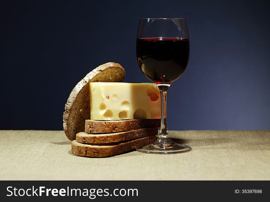 Still life with one goblet of red wine near sliced bread and cheese. Still life with one goblet of red wine near sliced bread and cheese