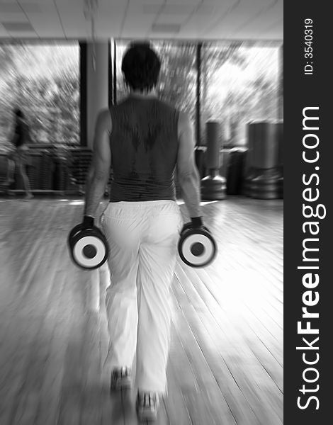 A man performs exercises for the legs in the gym with two dumbbells in the hands / Black and White with radial blur. A man performs exercises for the legs in the gym with two dumbbells in the hands / Black and White with radial blur