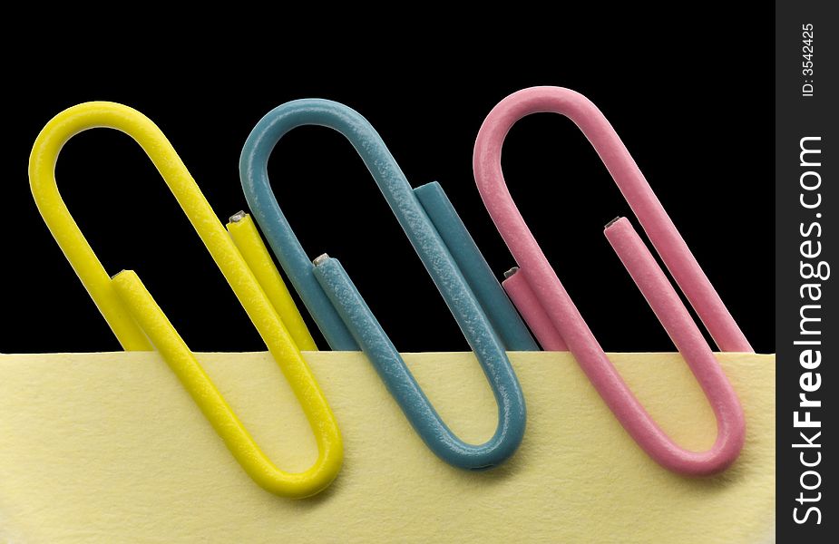 Paperclips on a yellow note with black background. Paperclips on a yellow note with black background