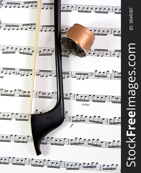 A black carbon fiber double bass bow and rosin on a piece of sheet music. A black carbon fiber double bass bow and rosin on a piece of sheet music.