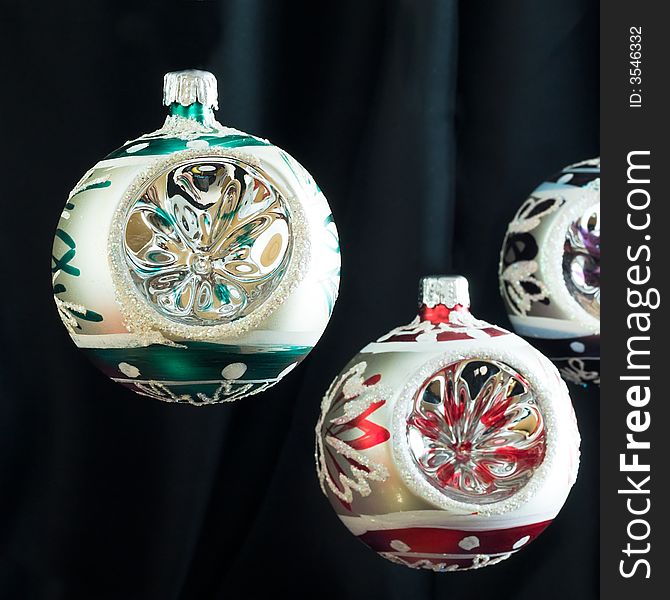 Three baubles of similar design but different colours suspended in the air against a black velvet background. Three baubles of similar design but different colours suspended in the air against a black velvet background
