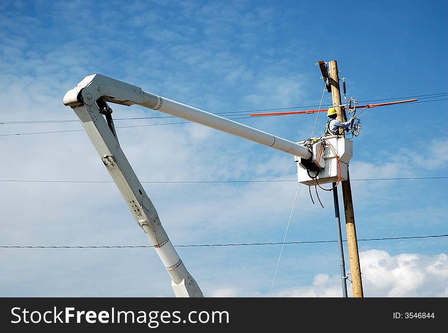 View of man in crane working on powerlines with blue sky in background. View of man in crane working on powerlines with blue sky in background