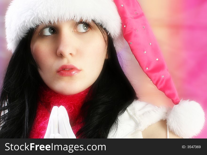 Beautiful young woman making Christmas wish. Wearing pink santa hat and white gloves.