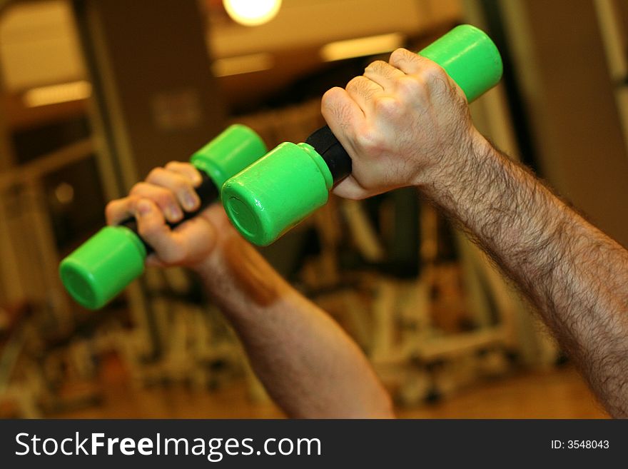 Two hands held close two green Dumbbells / Exercises in the gym / Blur Gym Background. Two hands held close two green Dumbbells / Exercises in the gym / Blur Gym Background